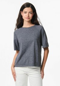 Maglione grigio leggero a maglia con maniche corte e scollo rotondo, caratterizzato da una texture morbida e una vestibilità comoda. Indossato con pantaloni di colore chiaro.