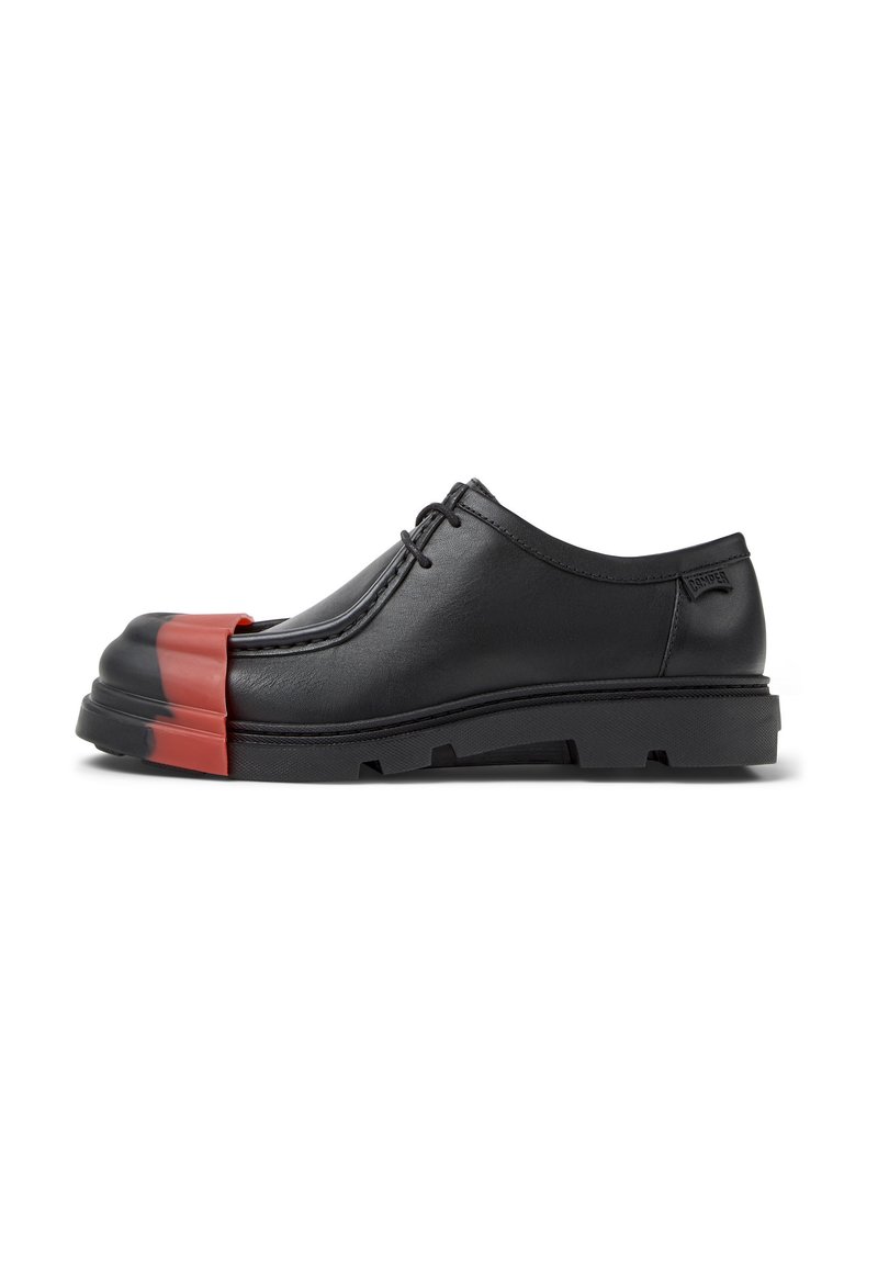 Zapatos de cuero negro con cordones que presentan una puntera redondeada con un acento rojo, suela gruesa y acabado texturizado. Diseño minimalista con marca lateral.