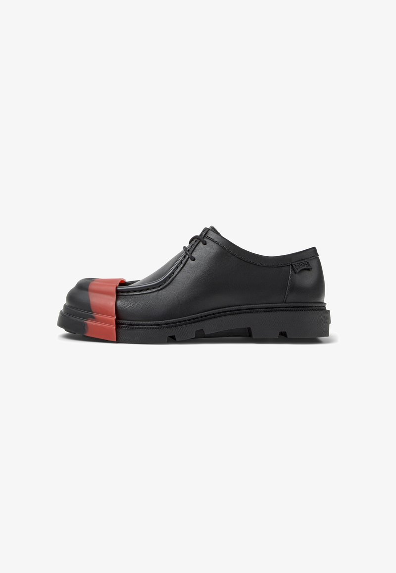 Zapatos de cuero negro con cordones que presentan una puntera redondeada con un acento rojo, suela gruesa y acabado texturizado. Diseño minimalista con marca lateral.