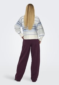 Gestrickter Pullover in Weiß und Blau mit geometrischen Mustern, kombiniert mit lockeren lila Hosen. Strukturierter Stoff und gerippte Bündchen.