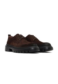 Brązowe zamszowe buty mają okrągły czubek, sznurowany design oraz grubą czarną gumową podeszwę z rowkowaną fakturą dla lepszej przyczepności.