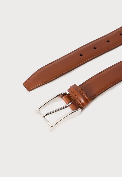 Ceinture en cuir marron posée à plat avec boucle métallique argentée et bords cousus sur un fond clair uni.