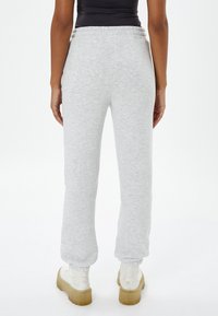 Pantalones de chándal grises hechos de material suave con un ajuste relajado, cinturilla elástica y puños ajustados, combinados con botas de plataforma blancas y voluminosas.