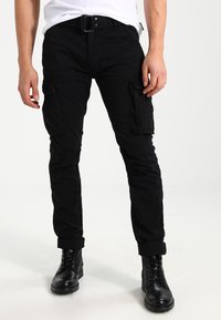 Zwarte cargo broeken met zijzakken, rechte snit en opgerolde cuffs, gecombineerd met zwarte veterschoenen en een wit t-shirt.