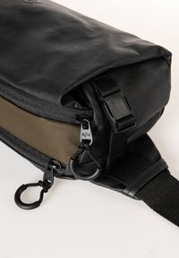 Borsa impermeabile nera con interni marroni, dotata di cerniere, spallacci regolabili e accessori metallici. Superficie testurizzata con cuciture robuste.