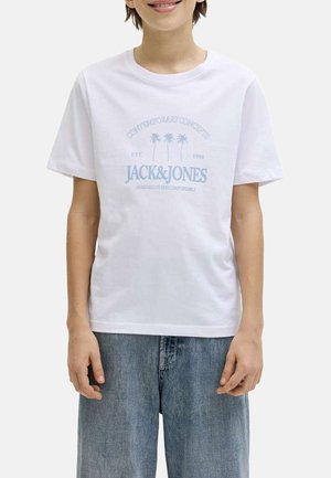 Persona vistiendo una camiseta blanca con texto "JACK & JONES" en azul claro y gráficos de palmeras, combinada con vaqueros azules holgados.