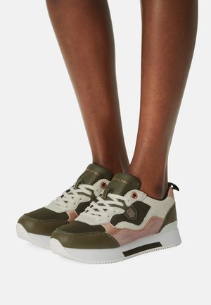 Primo piano di piedi che indossano sneakers Tommy Hilfiger verde, beige e rosa con suole bianche e lacci su uno sfondo bianco.