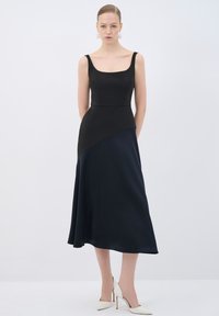 Ein ärmelloses schwarzes und dunkelblaues Kleid mit einem taillierten Oberteil und einem ausgestellten Rock, das ein asymmetrisches Farbblockdesign und eine glatte Textur aufweist.
