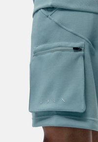 Pantalones cortos deportivos de color azul claro, hechos de una tela suave, con un bolsillo con cremallera en la pierna derecha y detalles minimalistas de la marca en blanco.