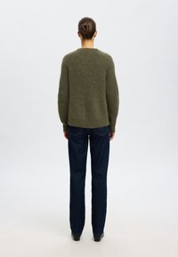 Grön, texturerad tröja med avslappnad passform, sänkt axel och rundad fåll, i kombination med mörkblå raka jeans.