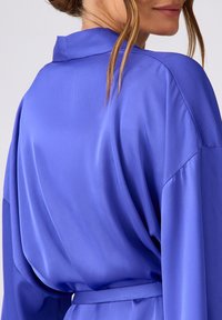 Szatynowy kimono w intensywnym niebieskim kolorze, z kołnierzykiem i długimi rękawami. Zawiera związany pasek, gładką teksturę oraz luźny krój z plisowanymi detalami.