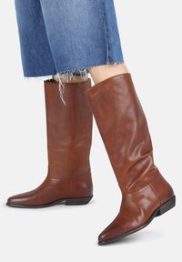 Botas de cuero marrón hasta la rodilla con punta afilada y tacón bajo. Textura suave con un ligero diseño arrugado y detalles de costura mínimos.