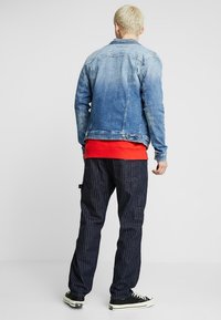 Jeansjacka i ljusblått, urtvättad design, tillsammans med en ljus röd skjorta. Mörka randiga byxor och svarta sneakers fulländar looken.