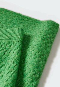 Grüner Pullover aus Strick mit strukturiertem Muster und gerippten Bündchen. Der Stoff wirkt weich und leicht und zeigt eine lebendige, gleichmäßige Farbe.