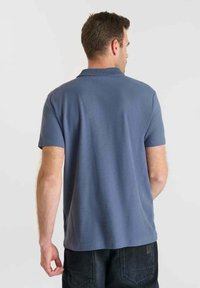 Polo à manches courtes, tissage texturé, couleur bleu foncé, col côtelé, coupe décontractée, porté avec un jean foncé, présenté de dos.