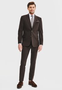 Brązowy garnitur z pasującymi spodniami, jasna koszula, wzorzysty krawat i poszetka. Brązowe buty dopełniają formalny strój.