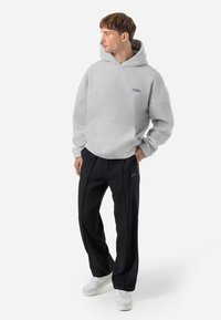 Lichtgrijze fleece hoodie met een grote capuchon en een voorzak, gecombineerd met zwarte broek en witte sneakers, met subtiele merkdetails.
