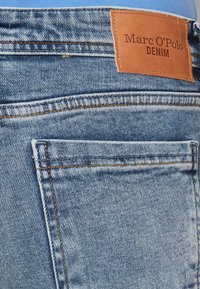 Siniset farkut, joissa on ruskea nahkainen etiketti, jossa lukee "Marc O'Polo DENIM", sekä yksityiskohtaista tikkausta taskuissa ja vyötärönauhassa.