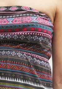 Top sin tirantes con una tela vibrante y estampada en negro, rosa, azul y blanco, con intrincados diseños geométricos y florales.