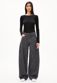 Schwarzes, tailliertes Langarmoberteil, kombiniert mit hochgeschnittenen, weit geschnittenen grauen Jeans aus Denim, die große Taschen und auffällige Nähte aufweisen.