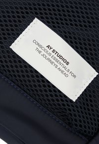 Marine meshstof med et hvidt mærke, der har sort tekst. Mærket står der "AY STUDIOS CONSCIOUS ESSENTIALS FOR THE JOURNEY AHEAD."