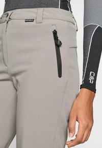 Heledad hallid püksid siledast kangast, küljepealne tõmblukuga tasku ja vöömärgiga; kantud musta ja halli pika varrukaga pluusiga, millel on kontrastsed detailid.