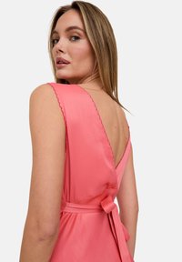 Rosa Satinkleid mit tiefem V-Rücken, geschwungenen Kanten an den Ärmeln und einem gebundenen Gürtel in der Taille, der einen sanften Fall erzeugt.