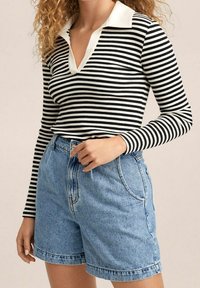 Camisa de manga larga a rayas blancas y negras con cuello blanco, combinada con pantalones cortos de mezclilla azul claro de cintura alta y con dobladillos enrollados.