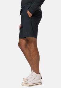 Mörkblå shorts i lättviktsmaterial med sidofickor och dragsko i midjan. En subtil logotyp är synlig på benet.