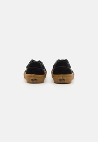 Crne nubuk cipele s bijelim šavovima, niskog profila, bez čipke i sa gumiranim potplatima, s "Vans" logotipom straga.