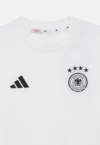 Λευκό βαμβακερό μπλουζάκι με μαύρο λογότυπο Adidas στο αριστερό στήθος και κυκλικό έμβλημα της Γερμανικής Ποδοσφαιρικής Ομοσπονδίας σε μαύρο και άσπρο με τέσσερις αστέρες.