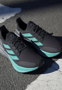 Black athletic shoes with turquoise accents, mesh upper, lacing system, and textured sole. Features three stripes on the side.