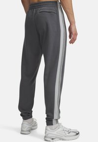Grå sweatpants med sidelange striber i lys grå og meleret grå. Elastisk linning og en lomme bagpå. Sæt sammen med hvide sneakers.