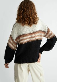 Maglione lavorato a maglia con strisce orizzontali in crema, beige e marrone, con una sezione inferiore nera e maniche oversize.