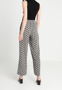 Haut sans manches noir associé à un pantalon large à motifs, présentant un design géométrique dans des tons bleus, crème et dorés. Texture lisse et coupe décontractée.