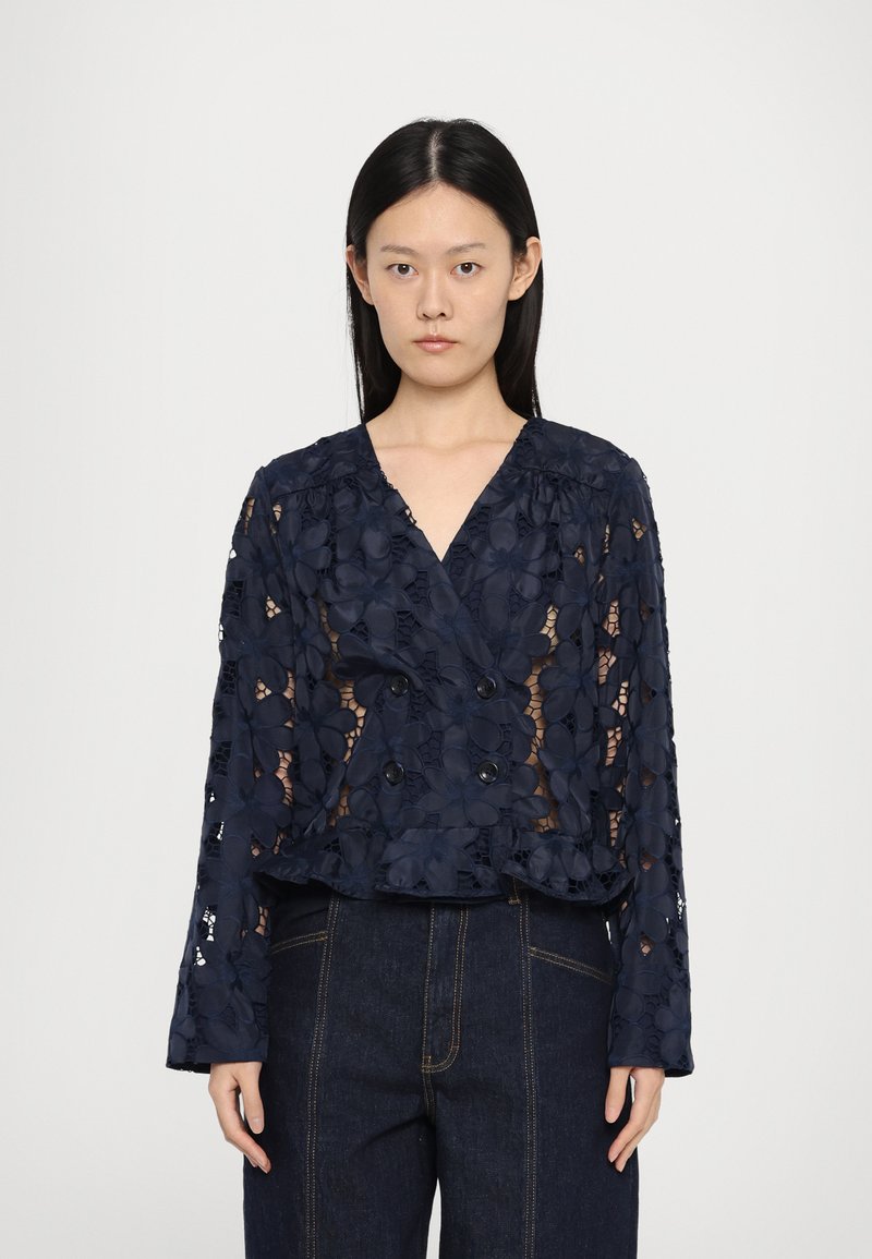 Navy blue blouse with floral lace details, double-breasted design, and long sleeves. Features a ruffled hem and sheer texture.