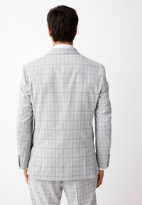 Chaqueta de traje gris a cuadros con corte ajustado. Presenta solapas de muesca, una abertura trasera y detalles de botones en las mangas. Tejido suave y texturizado.