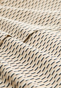 Tissu beige avec un motif répétitif de fines rayures navy et claires, présentant une texture lisse et une apparence légèrement froissée.