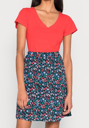 Haut rouge à manches courtes et col en V, associé à une jupe marine avec un motif floral multicolore et une taille élastique.