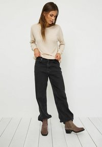 Beige lättvikts-hoodie med vid halsringning, kombinerat med högmidjade svarta jeans och bruna anklarstövlar med blockklack.