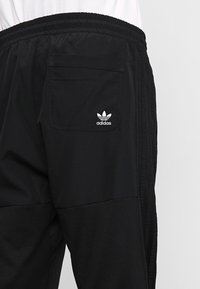 Svarta träningbyxor med texturerad tyg, sidosträck och bakficka. Adidas-logotypen syns i vitt på fickan.