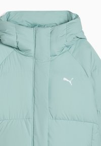 Lyseblå puffjakke med høj krave, vandret syninger, og et hvidt Puma-logo på brystet. Glat, vandafvisende stof.