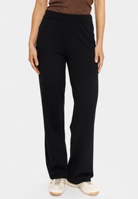 Juodos laisvos formos kelnės su pūkuota elastine juosmeniu. Medžiaga atrodo minkšta, turi lygų paviršių ir nematomas raštas.