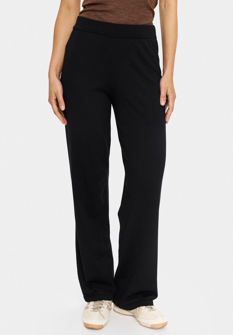 Juodos laisvos formos kelnės su pūkuota elastine juosmeniu. Medžiaga atrodo minkšta, turi lygų paviršių ir nematomas raštas.