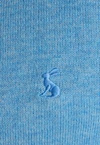 Blåt strikket stof med en lille broderet blå hare nær midten.