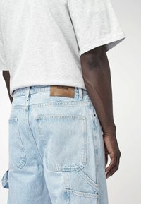 Vaaleansiniset farkkukangaspöksyt, joissa on useita taskuja, kontrastivärinen ommel ja ruskea nahkalappu. Puuvillasekoitetta, rento malli, keskimäinen vyötärö.