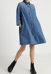 Jeansklänning med marinblå krage, knapp-fram, trekvartsärmar och sidfickor. Buren med svarta ankelboots.