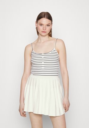 Top sin tirantes con rayas blancas y azul marino, que presenta tres botones en la parte delantera; complementado con una falda blanca de punto y plisada.