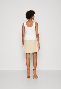 Hvid ærmeløs top med dyb ryg kombineret med en beige skorts. Båret med nude hælede ankelstøvler med en glat overflade.