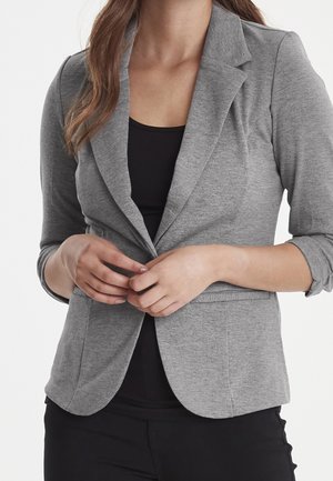 Blazer en tricot gris avec une coupe slim, col cranté et manches trois-quarts. Il dispose de poches avant et d'une fermeture à boutons.